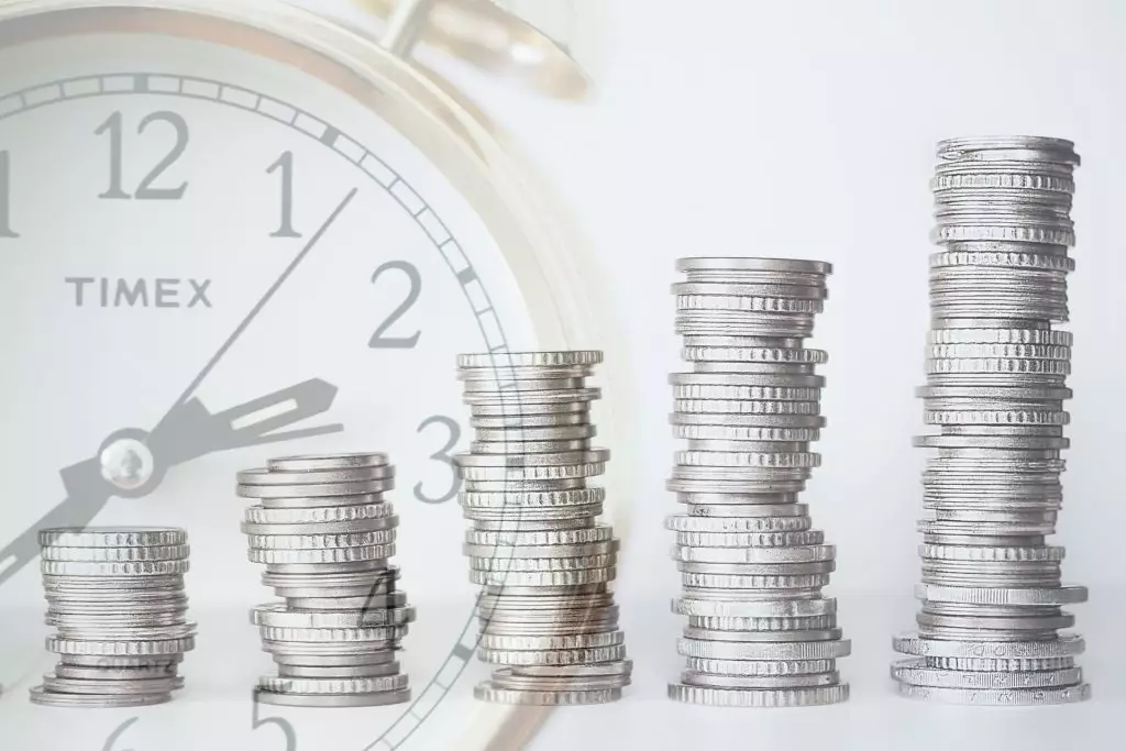 Coins stacked in front of clock representing the gains of period payments over time