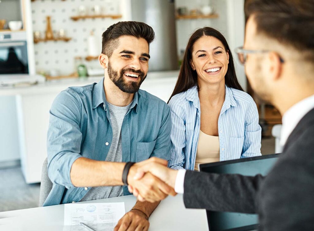 Two men shaking hands with a woman smiling beside them