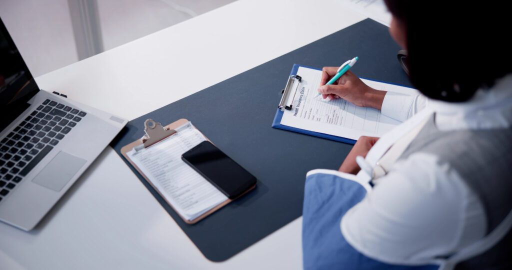 Professional completing a health insurance claim form, representing OasisFinancial.com’s commitment to helping patients manage medical expenses and claims.