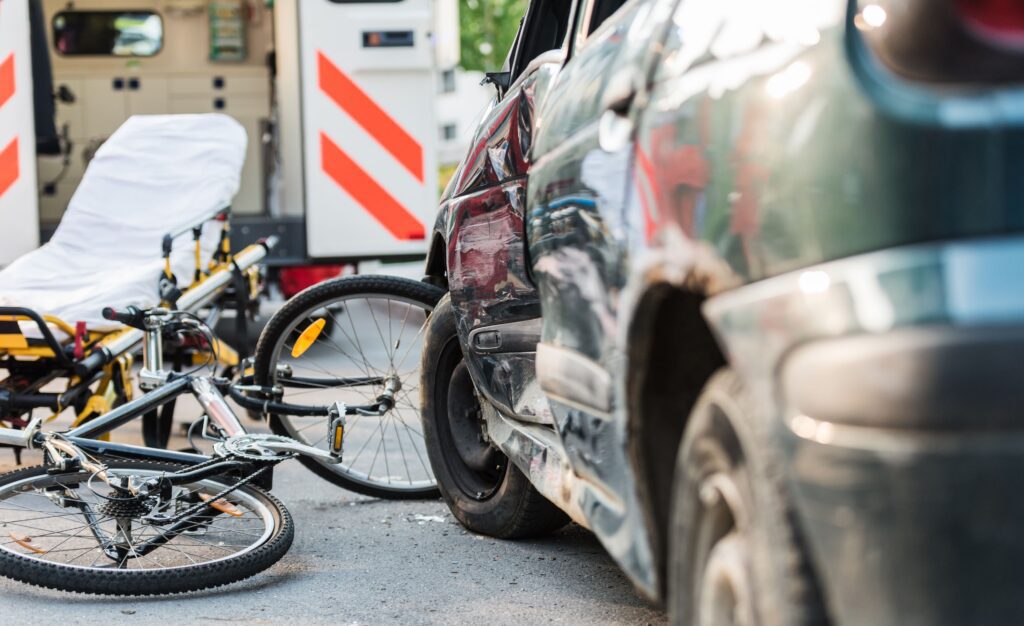 Damaged car, fallen bicycle, and an ambulance stretcher at the scene of a vehicle–cyclist accident