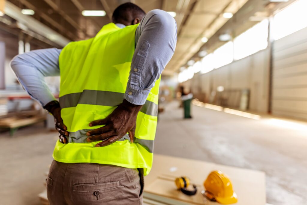 Injured worker in a safety vest holding their lower back